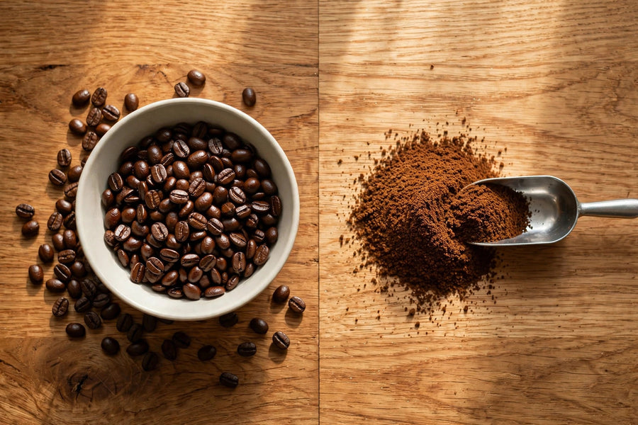 Whole coffee beans in a bowl beside a pile of freshly ground coffee